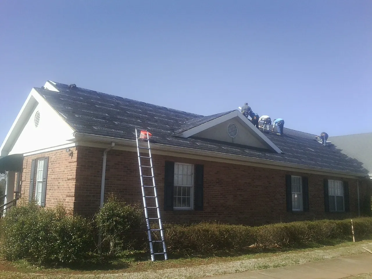 Crew tearing shingles off a brick ranch roof with a ladder set — Metal Roof Repair work by our crew in Hague