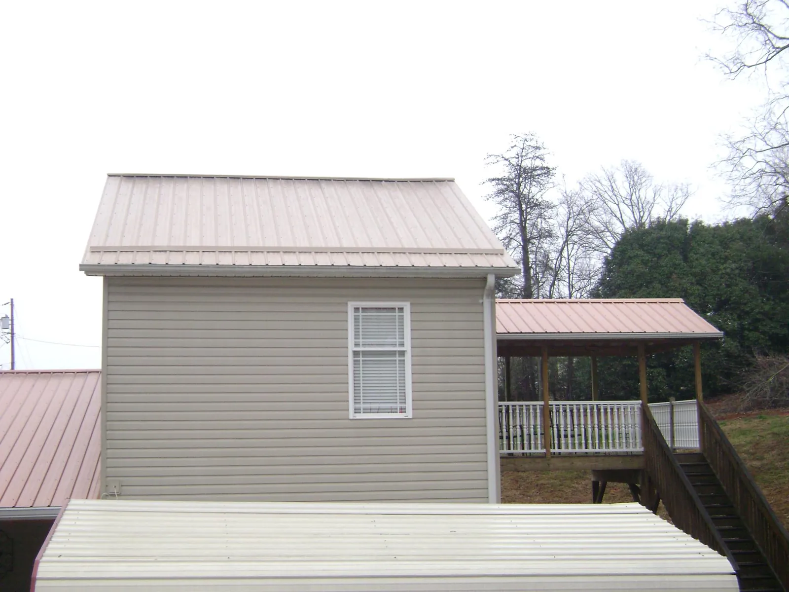 Tan metal roofs on a two story addition and attached porch, from a Roof Replacement job in Hague